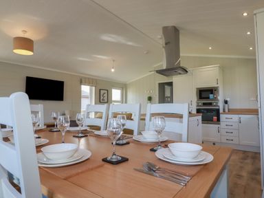 A dining table set with plates glassware and cutlery in a kitchen area with white cabinets and appliances at 4 Meadow Retreat in Dobwalls