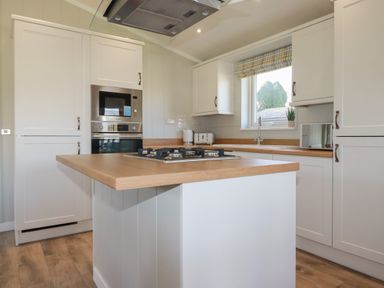A kitchen with white cabinets wooden countertops gas stove oven microwave and window at 4 Meadow Retreat in Dobwalls