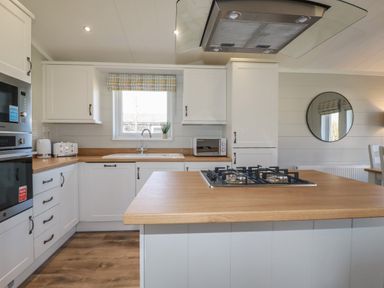A kitchen with white cabinets wooden countertops a gas stove a microwave toaster kettle and a window at 4 Meadow Retreat in Dobwalls