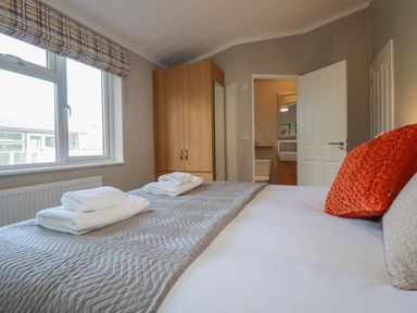 A bedroom with a bed with folded towels a wardrobe a window and an open door showing a bathroom at 4 Meadow Retreat in Dobwalls