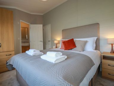 A bedroom with a bed with towels and pillows bedside tables with lamps and an open door showing a bathroom at 4 Meadow Retreat in Dobwalls