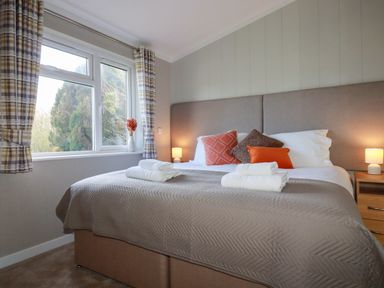 A bedroom with a double bed with folded towels bedside tables with lamps and a window with plaid curtains at 4 Meadow Retreat in Dobwalls