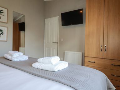 A bedroom with a bed with towels on it a wall mounted tv a wooden wardrobe and a door at 4 Meadow Retreat in Dobwalls