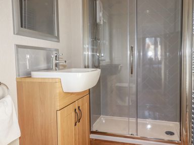 A bathroom with a wooden vanity cabinet with a white sink and a glass shower enclosure at 4 Meadow Retreat in Dobwalls