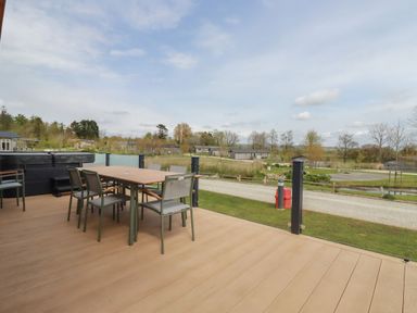 An outdoor deck with a dining table and chairs overlooking a grassy area and houses at 4 Meadow Retreat in Dobwalls
