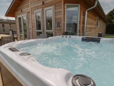 An outdoor hot tub with bubbling water next to a wooden house with windows and outdoor furniture at 4 Meadow Retreat in Dobwalls