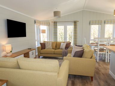 A living room with beige sofas a wall-mounted television and a dining table with chairs at 23 Meadow Retreat in Dobwalls