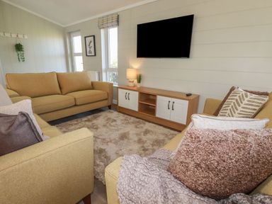 A living room with yellow sofas a mounted television a wooden cabinet and a beige rug at 23 Meadow Retreat in Dobwalls