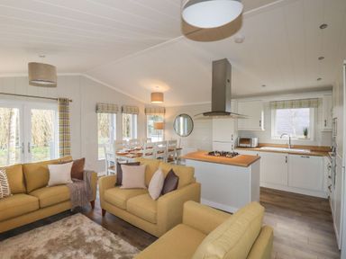 An open-plan living area with yellow sofas a dining table and a kitchen at 23 Meadow Retreat in Dobwalls