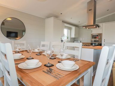 A dining table set with plates bowls cutlery and glasses in a kitchen with white cabinets and a round mirror at 23 Meadow Retreat in Dobwalls