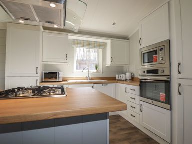 A kitchen with a gas stove on an island wooden countertop a microwave built into cabinetry a toaster kettle and a window at 23 Meadow Retreat Dobwalls