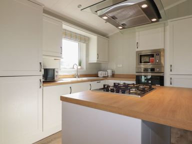 A kitchen with white cabinets a window with a checkered blind a gas stove on a wooden counter a microwave toaster and kettle at 23 Meadow Retreat in Dobwalls