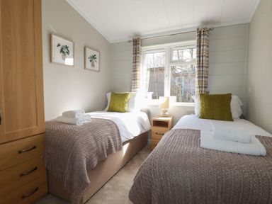A bedroom with two single beds with throws and green pillows a wooden wardrobe and nightstand with a lamp at 23 Meadow Retreat in Dobwalls