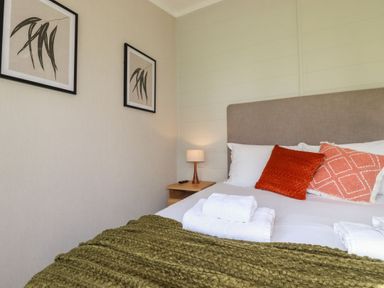 A bedroom with a bed with orange cushions white towels on a green blanket and framed plant prints on the wall at 23 Meadow Retreat in Dobwalls