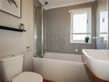 A bathroom with a toilet, bathtub with shower, sink, window, and a plant on the shelf at 23 Meadow Retreat in Dobwalls