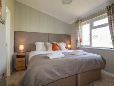 A bedroom with a double bed, bedside tables with lamps, and a window with curtains at 23 Meadow Retreat in Dobwalls