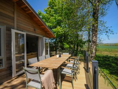 An outdoor wooden deck with a long table and chairs near a wooden house and trees at 23 Meadow Retreat in Dobwalls