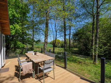 An outdoor wooden deck with a table and chairs surrounded by trees and glass railing at 23 Meadow Retreat in Dobwalls