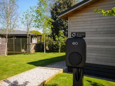 An outdoor electric vehicle charging station in front of wooden buildings with grass and trees at 23 Meadow Retreat in Dobwalls