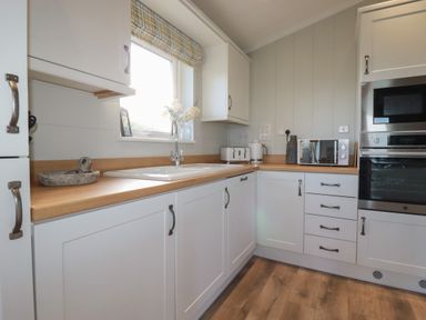 A kitchen with white cabinets wooden countertops a sink a window a toaster kettle microwave and oven at 6 Faraway Fields in Dobwalls