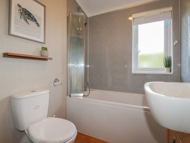 A bathroom with a toilet a bathtub with shower a sink and a window at 6 Faraway Fields Dobwalls