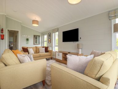 A living room with three beige sofas a wall mounted TV and a wooden TV stand at 6 Faraway Fields in Dobwalls