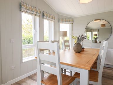 A dining room with a wooden table and white chairs a round mirror and a floor lamp at 6 Faraway Fields in Dobwalls