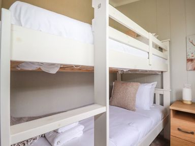 A bunk bed with white bedding and a pillow next to a wooden nightstand with a lamp at 6 Faraway Fields in Dobwalls