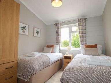 A bedroom with two single beds a window with curtains and a wooden wardrobe at 6 Faraway Fields in Dobwalls