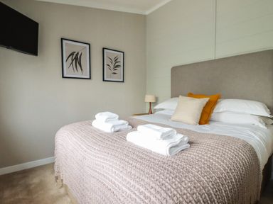 A bedroom with a bed with pillows and folded towels a bedside lamp two framed pictures and a wall-mounted television at 6 Faraway Fields in Dobwalls
