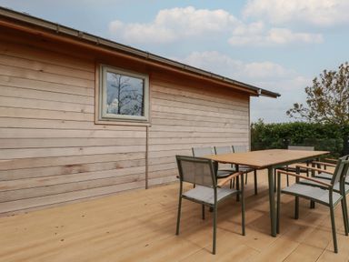 An outdoor wooden deck with a table and six chairs next to a wooden building at 6 Faraway Fields Dobwalls