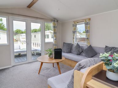 A living room with a round wooden table gray sofas and patio doors at Windermere Lodge in Morecambe