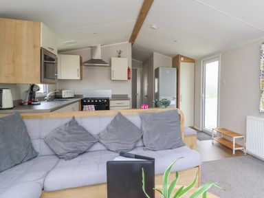 A kitchen and living area with a grey cushioned sofa and grey pillows at Windermere Lodge in Morecambe