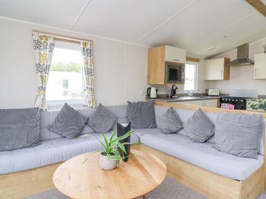 A living area with an L shaped sofa around a wooden coffee table and a kitchen visible in the background at Windermere Lodge in Morecambe