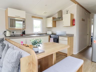 A kitchen and dining area with a sofa a wooden table microwave stove and refrigerator at Windermere Lodge in Morecambe
