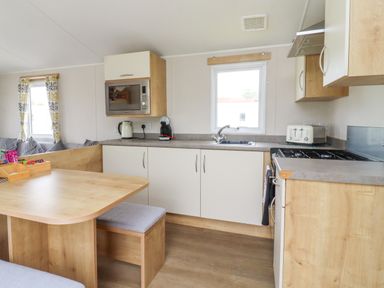 A kitchen with wooden cabinets a microwave kettle coffee machine toaster and a dining table at Windermere Lodge in Morecambe