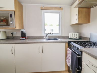 A kitchen with a sink below a window a microwave kettle coffee machine toaster and a stove with towels at Windermere Lodge in Morecambe