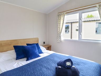 A bedroom with a bed with blue pillows and blanket and window with curtains at Windermere Lodge in Morecambe