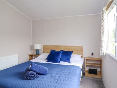 A bedroom with a double bed blue pillows blue bedspread bedside tables with lamp and window at Windermere Lodge in Morecambe
