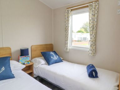 A bedroom with two single beds a nightstand a lamp and a window at Windermere Lodge in Morecambe