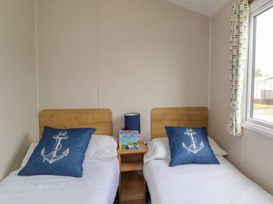 A bedroom with two single beds with wooden headboards and blue anchor pillows at Windermere Lodge in Morecambe