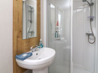 A bathroom with a sink a mirror a blue towel soap and a shower enclosure at Windermere Lodge in Morecambe