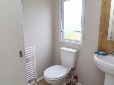 A bathroom with a toilet a sink a towel rail and a window at Windermere Lodge in Morecambe