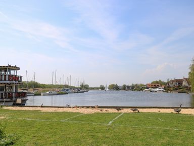 A river with boats docked on both sides and birds on grassy shore at Paws-A-While in Hoveton & Wroxham