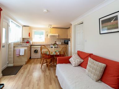 A kitchen with wooden cabinets a dining table with four chairs and an orange sofa with cushions at Paws-A-While in Hoveton & Wroxham