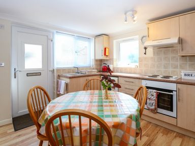 A kitchen with a round table covered by a colorful checkered tablecloth and four wooden chairs at Paws-A-While in Hoveton & Wroxham
