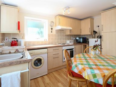 A kitchen with a round table covered with a colorful tablecloth and wooden chairs at Paws-A-While in Hoveton & Wroxham