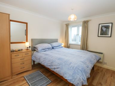 A bedroom with a double bed bedside tables a chest of drawers and a window at Paws-A-While in Hoveton & Wroxham