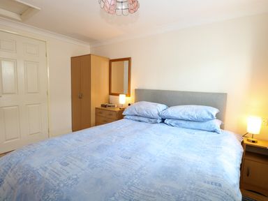 A bedroom with a double bed a wardrobe a chest of drawers and two lamps at Paws-A-While in Hoveton & Wroxham