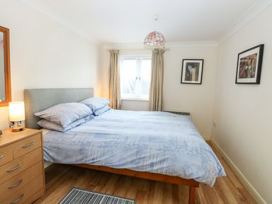 A bedroom with a double bed next to a wooden dresser and two framed pictures on the wall at Paws-A-While in Hoveton & Wroxham